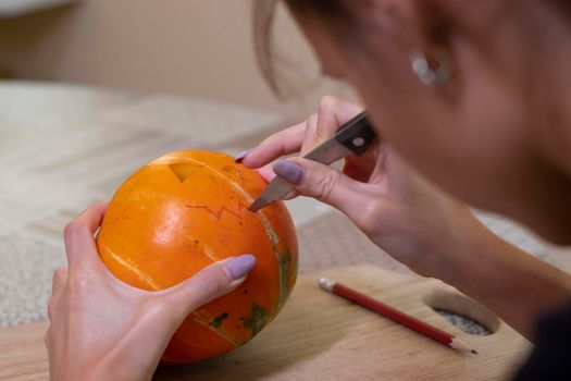 the process of making a Halloween pumpkin. cutting out the mouth by brunette girl. horror theme and Hallowe'en.