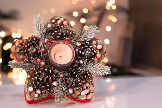 Christmas decor star-shaped made of tree branch with new years toys on it and a candle in it.