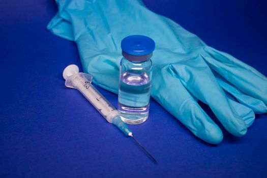 Vaccine bottle phial with no label, medical syringe with injection needle, blue medical gloves . isolated on blue background. cure. Development of coronavirus vaccine COVID-19. copy space