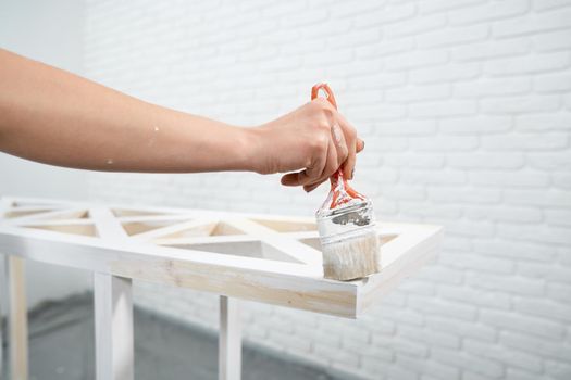 Close up of painting wooden rack in white color at home. Concept of repair.