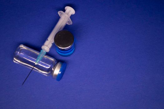 two transparent Vaccine bottle phial with no label, medical syringe injection needle. isolated on blue background. Development of coronavirus vaccine COVID-19. World race in researching. copy space