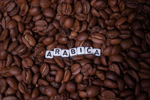 close up of Freshly roasted coffee beans near word ARABICA written with little white cubes. view from top