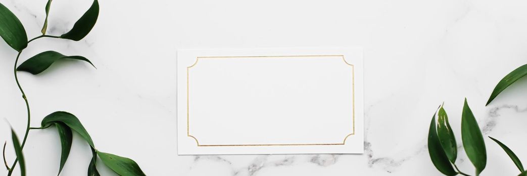 Blank white and gold card, green leaves on white background as botanical frame flatlay, wedding invitation and branding, flat lay design concept