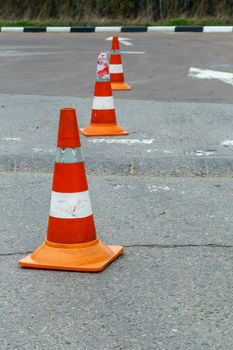 orange traffic cones on dry gray asphalt road surface - close-up with selective focus.