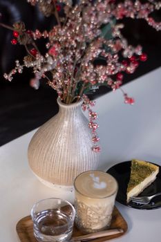 cup of coffee latte or cappuccino with piece of cake near vase with decorative red branches. interior, cozy. copy space