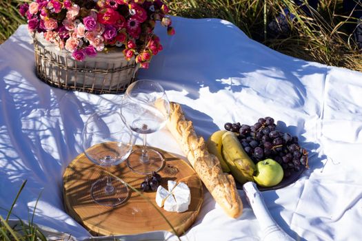 wooden stand with two glasses of champagne, grapes, baguette and camembert cheese on a white blanket in the field. picnic.