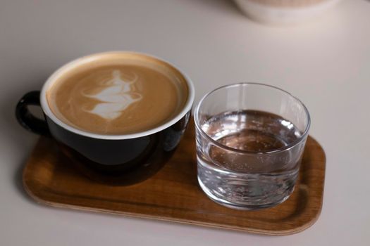 cup of coffee latte or cappuccino with glass of water on wooden tray. interior, cozy. copy space