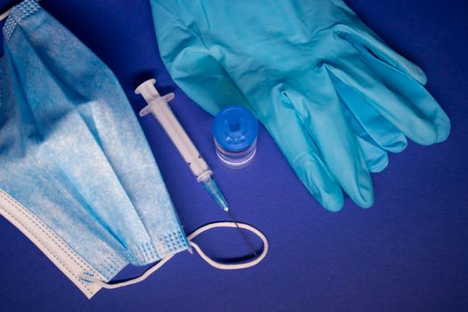 Vaccine bottle phial with no label, medical syringe with injection needle, blue medical mask and gloves . isolated on blue background. cure. Development of coronavirus vaccine COVID-19. copy space