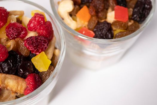 muesli dessert with yogurt and candied or dried fruits with raspberries on top in glass isolated on white background. breakfast Granola