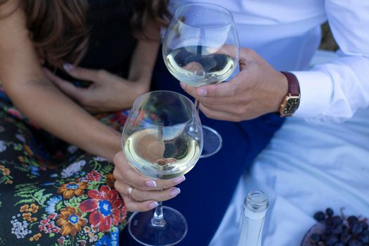 two hands -man's and women's holding champagne glasses on white blanket. picnic.