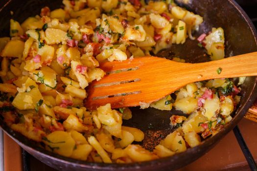 roasted domestic potatos in a frying pan with wooden spatula close-up with selective focus.