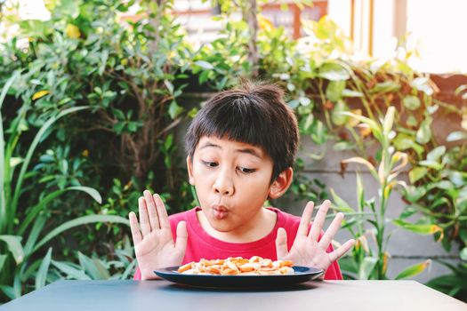 Cute Asian child in a red shirt showed a good expression when he saw a pizza in a plate placed in front of the table.