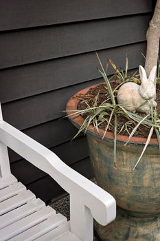 A ceramic bunny rabbit and a little blue bird in a garden pot plant beside a painted white chair