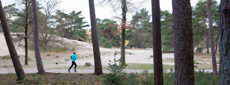 woman jogging in forest of province utrecht in holland near pine trees and sand dunes