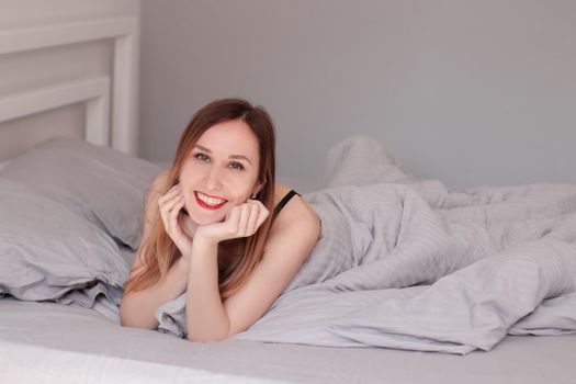 pretty redhead woman in black lace lingerie on bed with grey sheets.