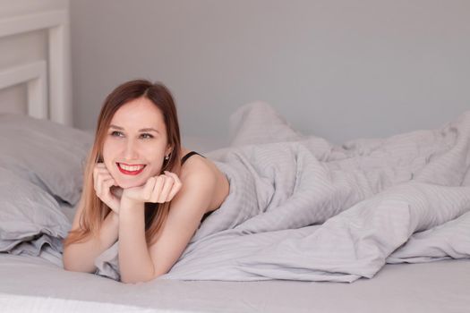 pretty redhead woman in black lace lingerie on bed with grey sheets.