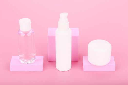 High angle view of skin lotion in transparent bottle, face cream and lip balm or under eye cream against pink background.