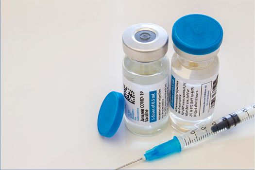 Calgary, Alberta, Canada. April 21, 2021. A couple of Janssen Covid-19 vaccine made by Johnson and Johnson. Vaccine vials bottles and an injection syringe on a clear table.