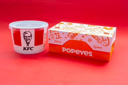 Calgary, Alberta, Canada. May 5, 2021. KFC and Popeyes Fast food boxes on a red background.
