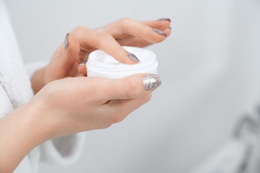 Side view close up of young woman holding cream for face or body in bathroom. Concept of preparing for using special cream for improvements skin and for care body.