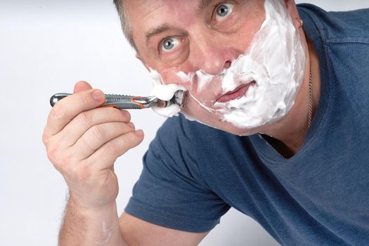 A man's face in shaving foam shaves with a safety razor. Morning or evening exercise, personal hygiene