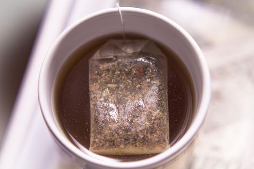 White cup with infusion and tea bag. No people