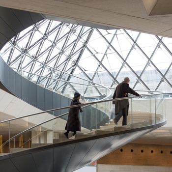 Paris, France - February 20 2014: Elderly man and woman climb spiral staircase at  the atrium The Louvre Paris