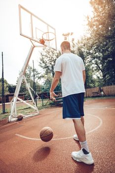 Young man is training basketball on street court. He is ready to take the ball.
