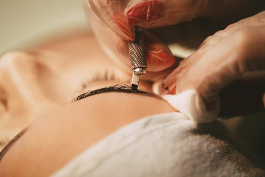 Close-up of a beautician hands applying permanent eyebrow makeup to model.  