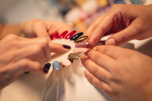 Close-up of a beautician and female clients hands holding samples and choosing colours nails at the beauty salon.