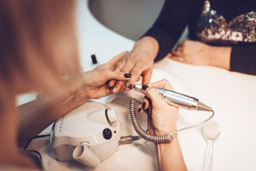 Beautician polishing female clients nails with nail file at the beauty salon.