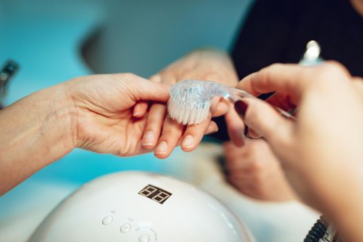 Close-up of a beautician brushing female clients nails for manicure process at the beauty salon.