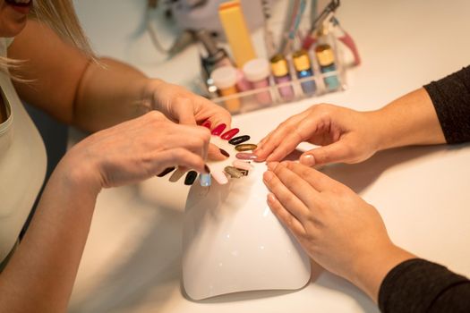 Close-up of a beautician and female clients hands holding samples and choosing colours nails at the beauty salon.
