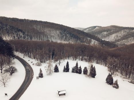 Drone aerial top view of a road going through forest with snow.