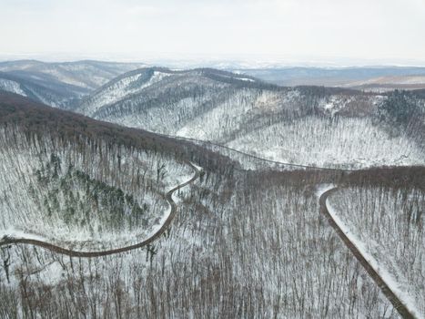 Drone aerial top view of a road going through forest with snow.