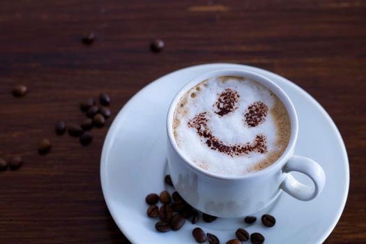 A cup of hot coffee with a picture of a smile on a wooden table.