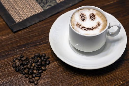 A cup of hot coffee with chocolate chips on a wooden table.