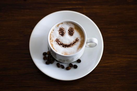 Coffee with milk and a smile in a cup. Lots of coffee beans on the table. Place for your text.