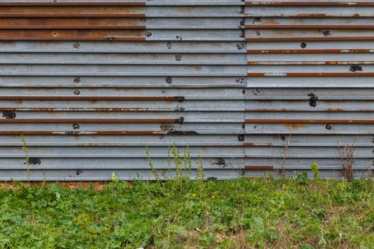 rusted corrugated steel sheets with leftovers of zync plating background and texture with ground and grass underneath