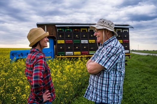 Proud two generations beekeepers are standing in front of their truck with beehives.