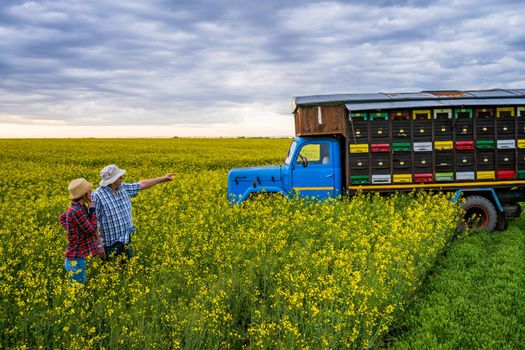 Proud two generations beekeepers are standing in front of their truck with beehives.