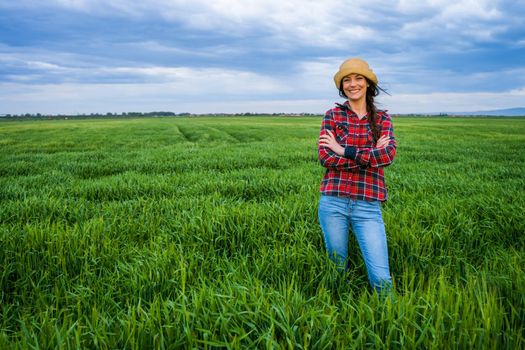 Proud female farmer is standing in her barley field and enjoying sunset.