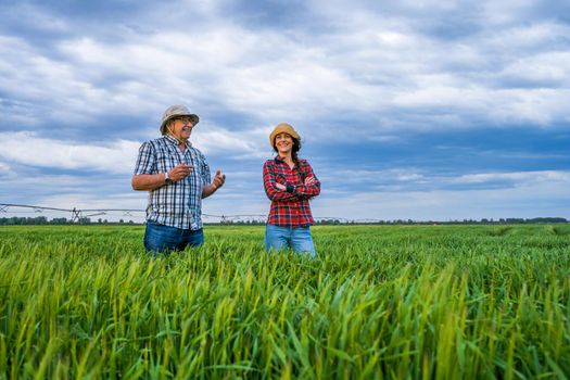 Proud two generations farmers are standing in their barley field and examining crops. Senior man is educating his successor about the farming.