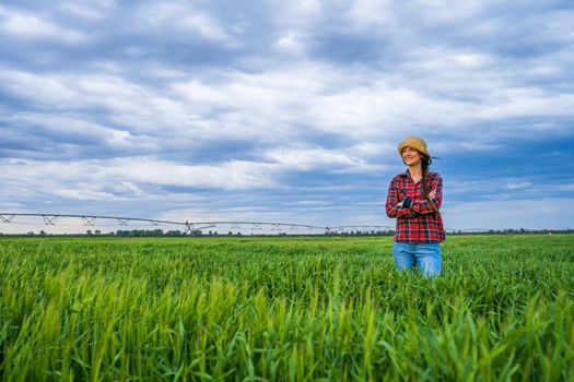 Proud female farmer is standing in her barley field and enjoying sunset.