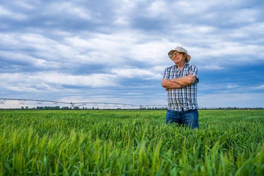 Proud senior farmer is standing in his barley field and enjoying sunset.