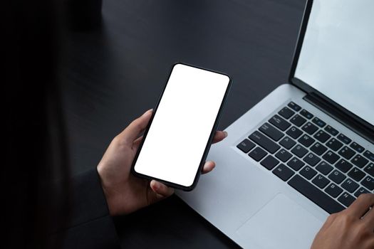 Shot of woman holding blank screen mock up mobile phone during typing on laptop computer