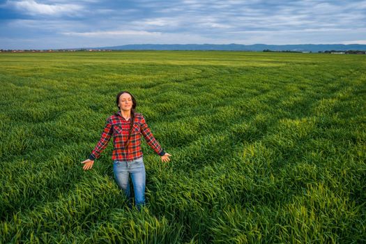 Proud female farmer is standing in her barley field and enjoying sunset.