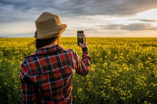 Proud female farmer is taking photo of her rapeseed field.