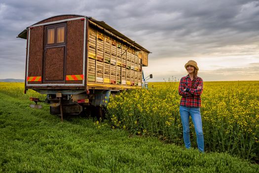 Proud female beekeeper is standing in front of her truck with beehives.