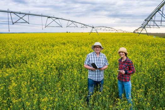 Proud two generations farmers are standing in their rapeseed field and examining plants.